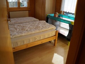 A wooden bed with a mattress and a child standing by a window. - Dilaila, (Grächen), by Interhome (Grächen)