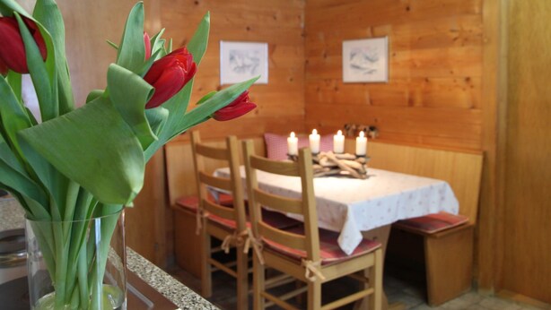 Puisesti sisustettu tila, jossa on ruokapöytä, tuoleja, kynttilöitä ja maljakko, jossa on punaisia tulppaaneja.
