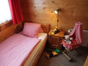 Een gezellige kamer met een enkel bed, een nachtkastje, een lamp en een teddybeer in een mandje.