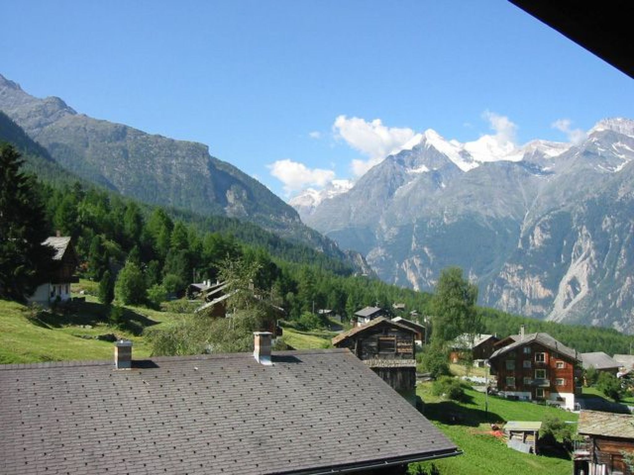 A mountain village with traditional wooden houses, a clear sky, and snow-capped peaks in the background.