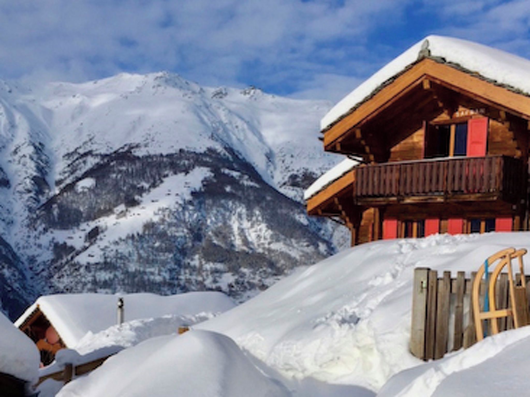 A wooden chalet with a balcony, surrounded by snow-covered mountains.