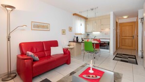 Un salon moderne avec un canapé rouge, un pouf noir et une table basse blanche sur laquelle est posée une bougie.