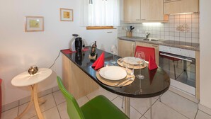 Une cuisine compacte avec un coin repas, équipée d’une machine à café, de verres à vin et d’une petite table dressée pour deux personnes.