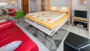 Une chambre moderne avec un lit double, un canapé rouge, une télévision et un coin cuisine.