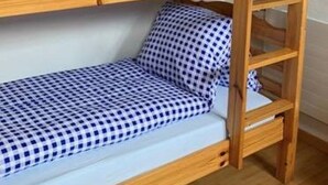 Un lit superposé avec une literie à carreaux, une structure en bois et une petite étagère sous le lit du haut.