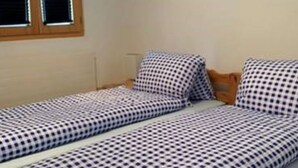 Une chambre avec deux lits simples, chacun recouvert d’une courtepointe à carreaux, doté d’une tête de lit en bois et d’une fenêtre avec des stores.