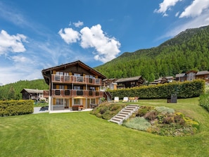 Ein mehrgeschossiges Chalet mit Balkonen, umgeben von einem gepflegten Garten und einer Bergkulisse.