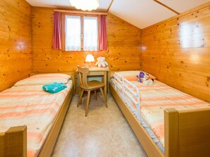 Eine Holzhütte mit zwei Etagenbetten, einem Schreibtisch mit Stuhl, einem Fenster mit Vorhängen und einem Teddybären auf dem Schreibtisch.