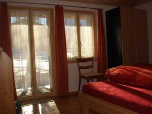 A bedroom with a bed, a chair, and a window with curtains. - Chalet Petunia, (Grächen), 1116 by Interhome (Grächen)