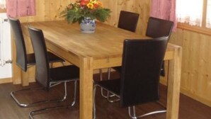 A wooden-paneled room with a wooden dining table, black chairs, a vase of flowers, and a clock on the wall. - Chalet Petunia, (Grächen), 1116 by Interhome (Grächen)