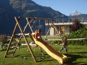 Un terrain de jeux équipé d’un toboggan et d’une structure d’escalade, le tout situé dans un cadre montagneux.