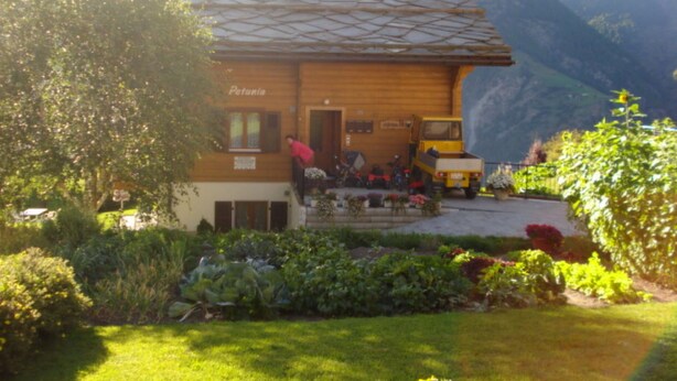 A wooden building with a tiled roof, a sign reading 'Patania,' and a vehicle parked outside. - Chalet Petunia, (Grächen), 1116 by Interhome (Grächen)