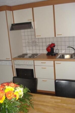 Een keuken met witte kastjes, een zwarte kookplaat en een rode koffiezetapparaat.
