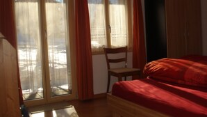 A bedroom with a bed, a chair, a wardrobe, and a window with curtains. - Chalet Petunia, (Grächen), 1116 by Interhome (Grächen)