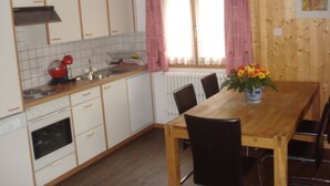 A kitchen with white cabinets, a red mixer, and a wooden dining table with chairs. - Chalet Petunia, (Grächen), 1116 by Interhome (Grächen)