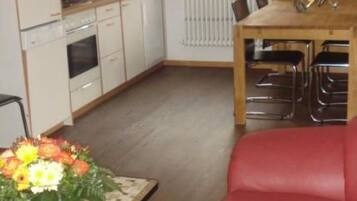 A compact kitchen with white cabinets, a dining table with chairs, and a red sofa.