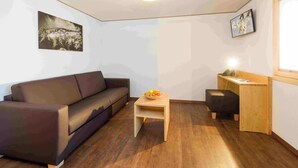 A small living room with a sofa, a small table with fruit, a desk, and a picture on the wall. - Lunic, AZapartments.ch, B&B, (Grächen), 1057 by Interhome (Grächen)