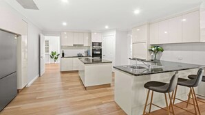 Cozinha moderna com armários brancos, uma ilha central com banquetas, uma geladeira de aço inoxidável e um micro-ondas.