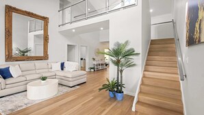 Uma sala de estar moderna com sofá, mesa de centro e plantas, uma escada e um espelho grande.