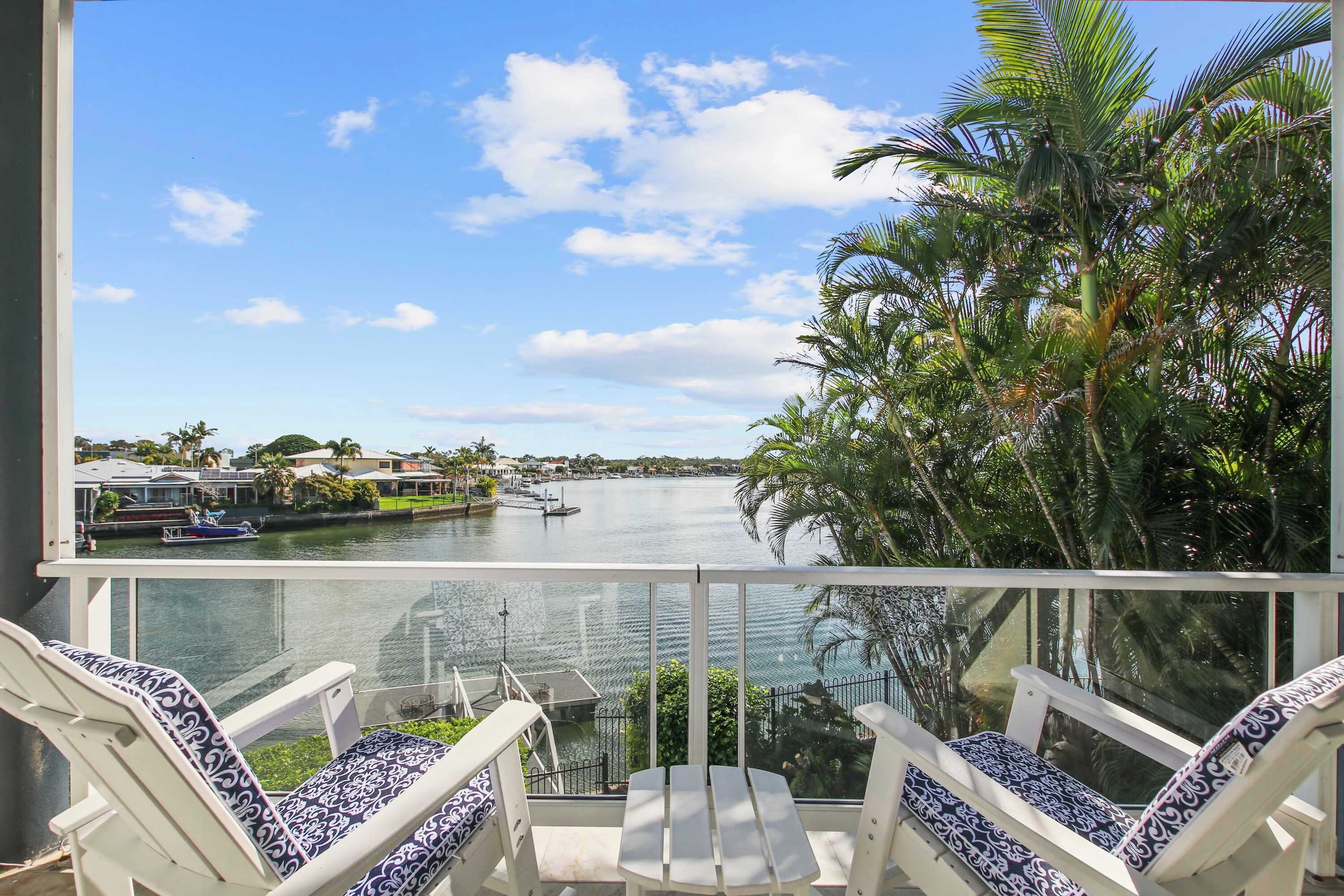 A balcony with two chairs and a table, overlooking a body of water with boats and a marina.