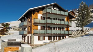 Ein mehrstöckiges Hotel mit Balkonen, ein Skiabhang im Hintergrund und eine schneebedeckte Landschaft.