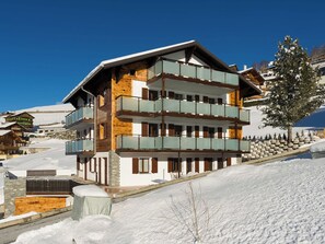 A multi-story hotel with balconies, a ski slope in the background, and a snow-covered landscape. - Lunic, AZapartments.ch, B&B, (Grächen), 1057 by Interhome (Grächen)