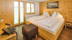 Ein Zimmer mit Holzwandverkleidung, einem Bett, einem Schreibtisch mit Telefon und einer Bank.