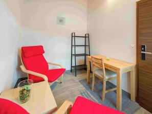 A small room with a red chair, a wooden table, and a black shelf unit. - Lunic, AZapartments.ch, B&B, (Grächen), 1057 by Interhome (Grächen)