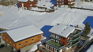 Um complexo de edifícios coberto de neve, com várias estruturas, incluindo um edifício de madeira grande e um menor com telhado verde.