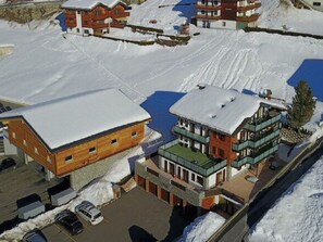 A snow-covered building complex with multiple structures, including a large wooden building and a smaller building with a green roof. - Lunic, AZapartments.ch, B&B, (Grächen), 1057 by Interhome (Grächen)