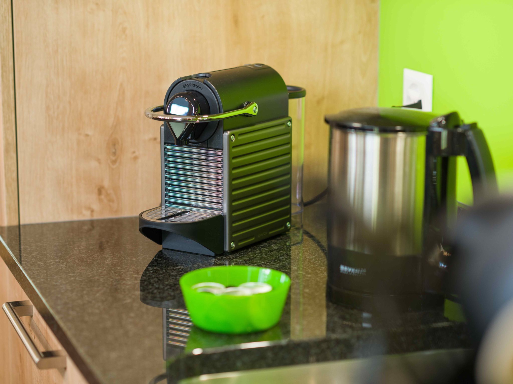 Máquina de café numa bancada de cozinha, com uma tigela verde e uma chaleira.