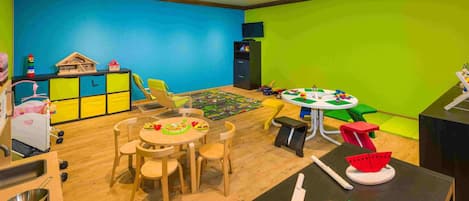 A children's playroom with a round table, chairs, and various toys.