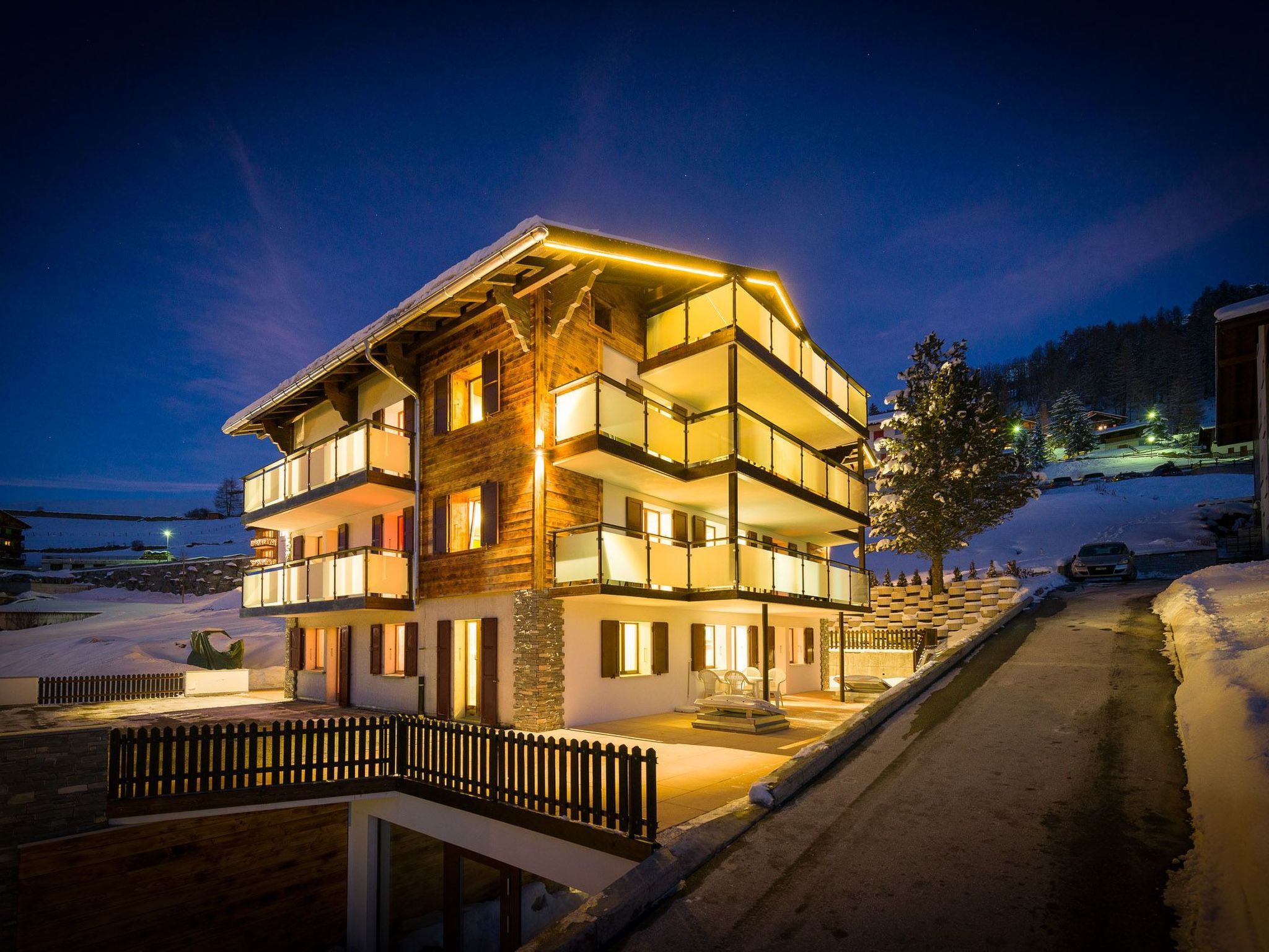 Un immeuble à plusieurs étages, doté de balcons et d’une façade en bois, se dressant au milieu d’un paysage enneigé, au crépuscule.