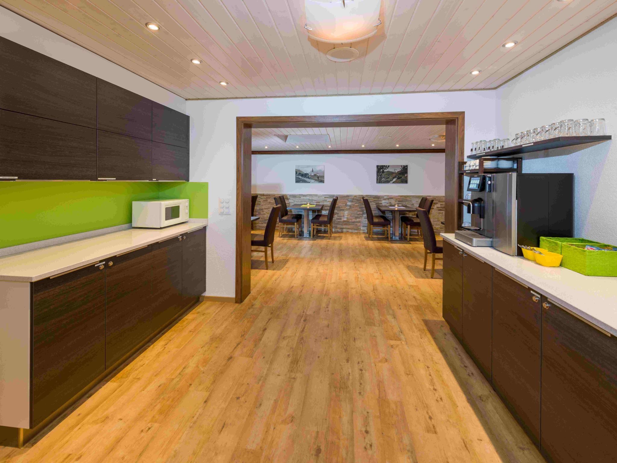 A modern kitchen with wooden flooring, built-in cabinets, a microwave, and a coffee machine.