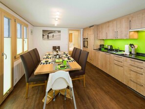 A dining area with a wooden table set for four, flanked by wooden cabinets and a green backsplash in the adjacent kitchen. - Ferienwohnungen Lunic, AZapartments.ch, B&B, (Grächen), 1057 by Interhome (Grächen)