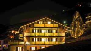 Ein mehrstöckiges Gebäude mit Balkonen und beleuchteten Fenstern, eingebettet in eine verschneite Landschaft.