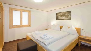 Ein Schlafzimmer mit einem hölzernen Bett, einer Sitzbank, einem Nachttisch, einem Fenster mit Jalousien und einem Wandbild.