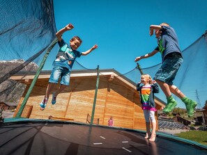 A trampoline with netted safety barriers, wooden flooring, and a clear blue sky in the background. - Ferienwohnungen Lunic, AZapartments.ch, B&B, (Grächen), 1057 by Interhome (Grächen)