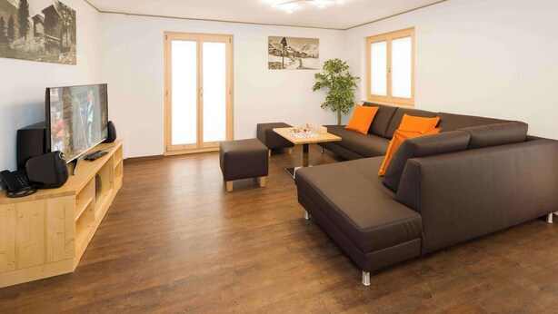 Ein modernes Wohnzimmer mit einer Couch, einem Hocker und einem Fernseher auf einem Holzboden.