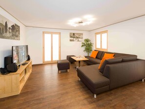 A modern living room with a sectional sofa, a wooden entertainment unit, and a dining area. - Ferienwohnungen Lunic, AZapartments.ch, B&B, (Grächen), 1057 by Interhome (Grächen)