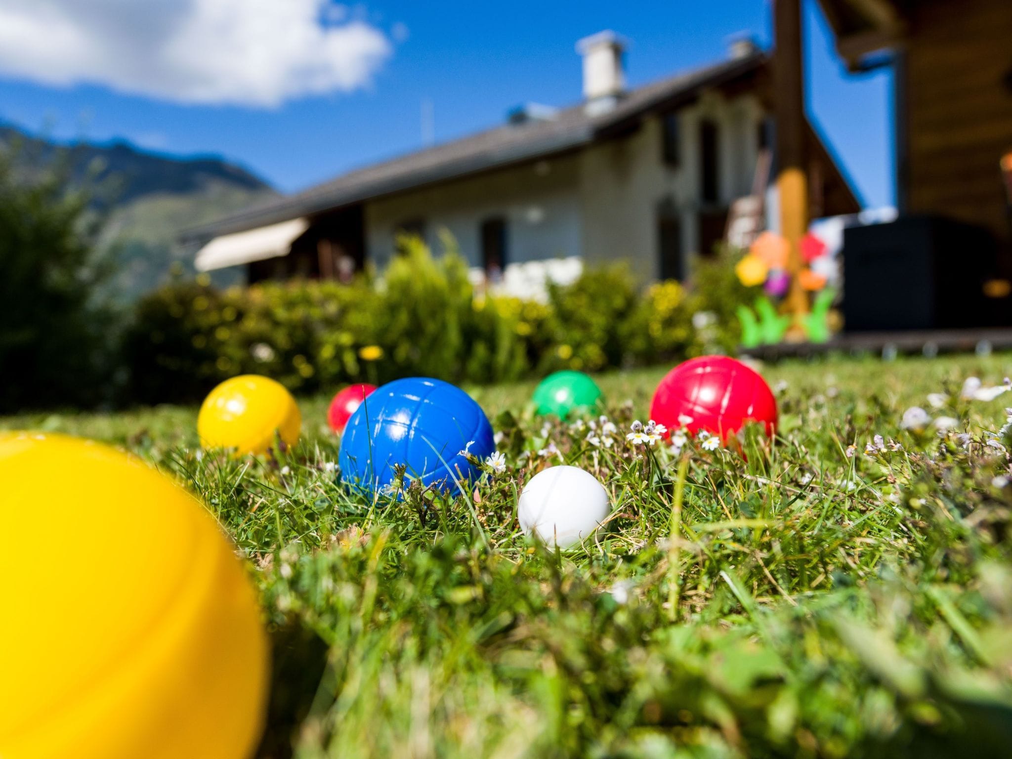 Colorful balls on grass with a house and mountains in the background.