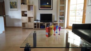 A living room with a flat-screen TV, wooden shelving, a glass coffee table, and a black leather sofa. - Thea, (Grächen), 1021 by Interhome (Grächen)