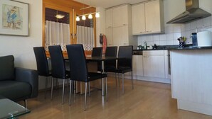 A modern kitchen with white cabinets, a dining table with chairs, and a small island with a sink. - Thea, (Grächen), 1021 by Interhome (Grächen)