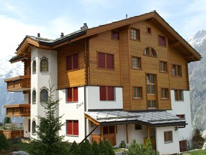 Ein mehrstöckiges Holzhaus mit Balkonen, roten Fensterläden und einem Berg im Hintergrund.