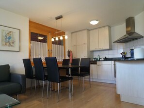 A compact kitchen with a dining area, featuring a table with chairs, a refrigerator, and cabinets. - Thea, (Grächen), 1021 by Interhome (Grächen)