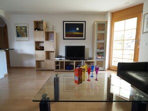 A living room with a glass coffee table, a flat-screen TV, wooden shelving, and a black leather sofa. - Thea, (Grächen), 1021 by Interhome (Grächen)