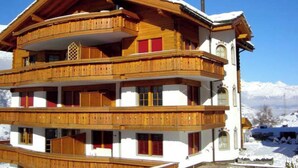 A multi-story wooden chalet with balconies, set against a snowy mountain backdrop. - Thea, (Grächen), 1021 by Interhome (Grächen)