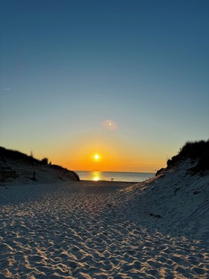 Ein Strand mit Sonnenuntergang, Sanddünen und blauem Himmel.