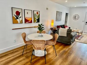 A modern living room with a round dining table, wicker chairs, a grey sofa, and a coffee table. - The Little Retreat | Entire Duplex | 4BR/4BA (Cape Charles)