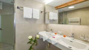 Un bagno moderno con due lavabi, cabina doccia in vetro e uno sgabello di legno con un vaso di fiori.